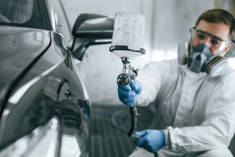 White protective wear. Man is painting a car by using spray guy